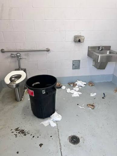 Neglected, messy commercial restroom with overflowing trash and dirty floor