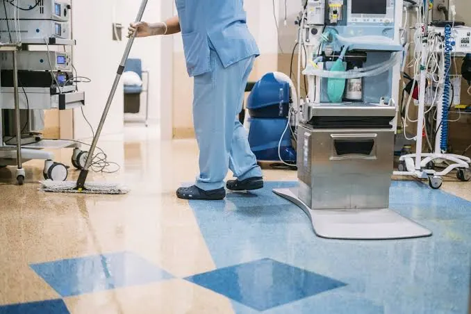 Cleaner mopping a medical facility floor beside equipment